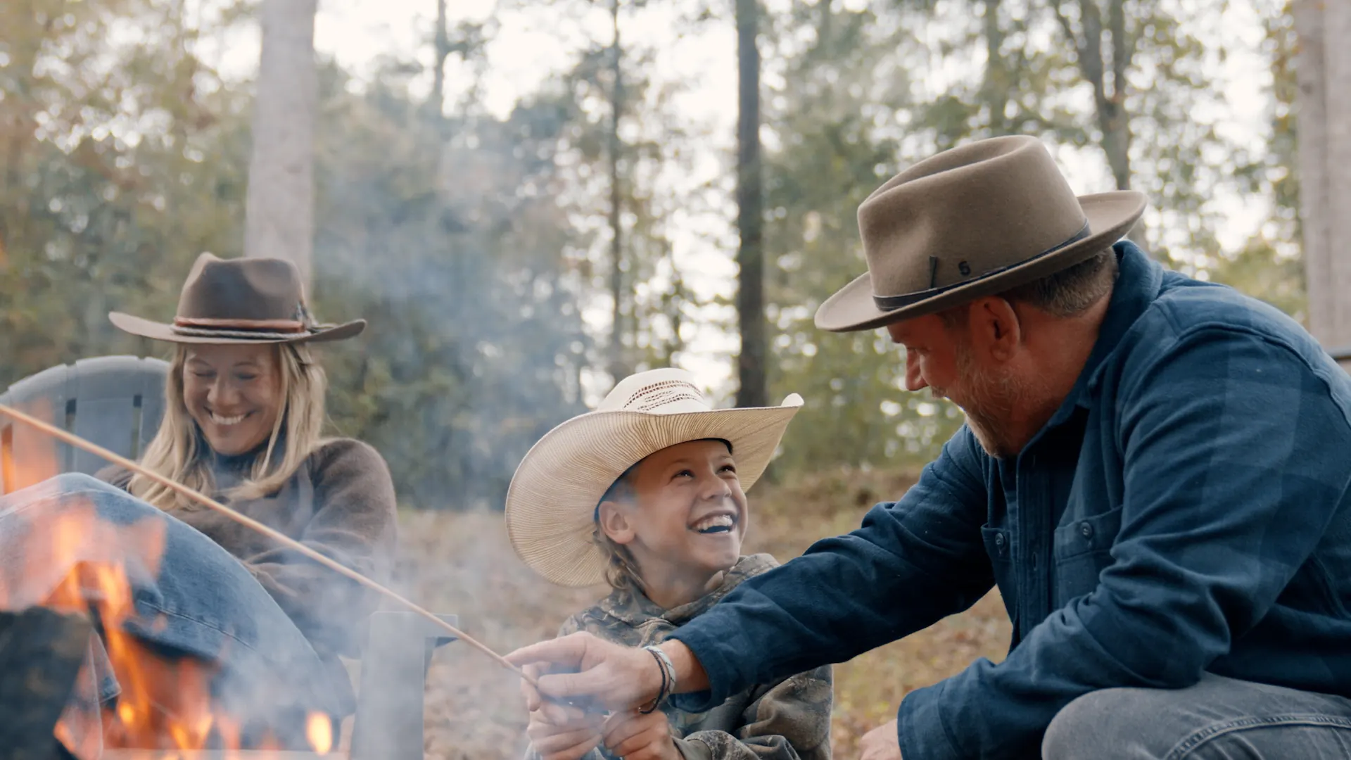 A family laughing around a campfire in the woods