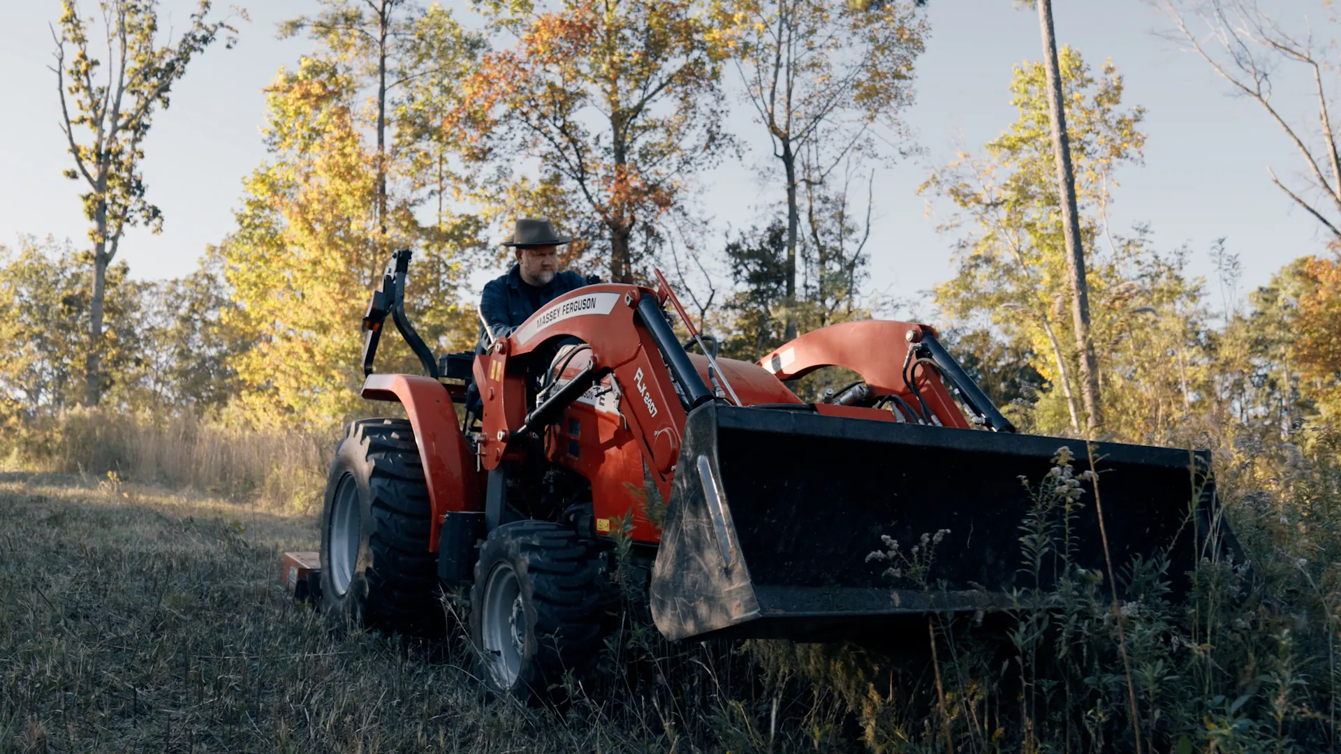 Clearing a meadow on a tractor, autumn trees behind